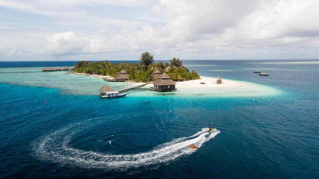 Tropu sala ar baltu smilšu pludmali un eksotisku veģetāciju, apņemta ar dzidru zilu ūdeni, kurā redzami ūdens motocikli un laivas. Pēcpusdienas debesis ar mākoņiem papildina šo idillisko ainavu.