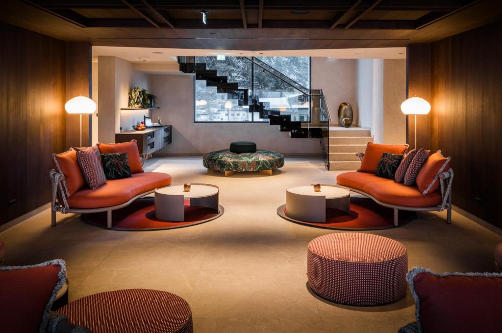 Mūsdienīgs viesnīcas interjers ar stilīgām sēdvietām un apgaismojumu. Telpā ir redzama eleganta kāpņu konstrukcija un dekoratīvi elementi, radot viesmīlīgu atmosfēru.