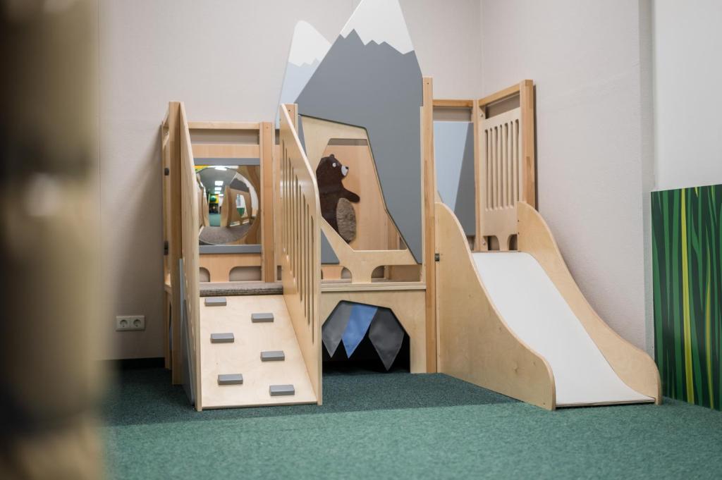 Bērnu rotaļu stacija ar koka struktūru, kas ietver kāpšanas elementus, slīdkalniņu un spoguli. Rotaļlaukums ir izveidots, lai veicinātu bērnu radošumu un fizisko attīstību.