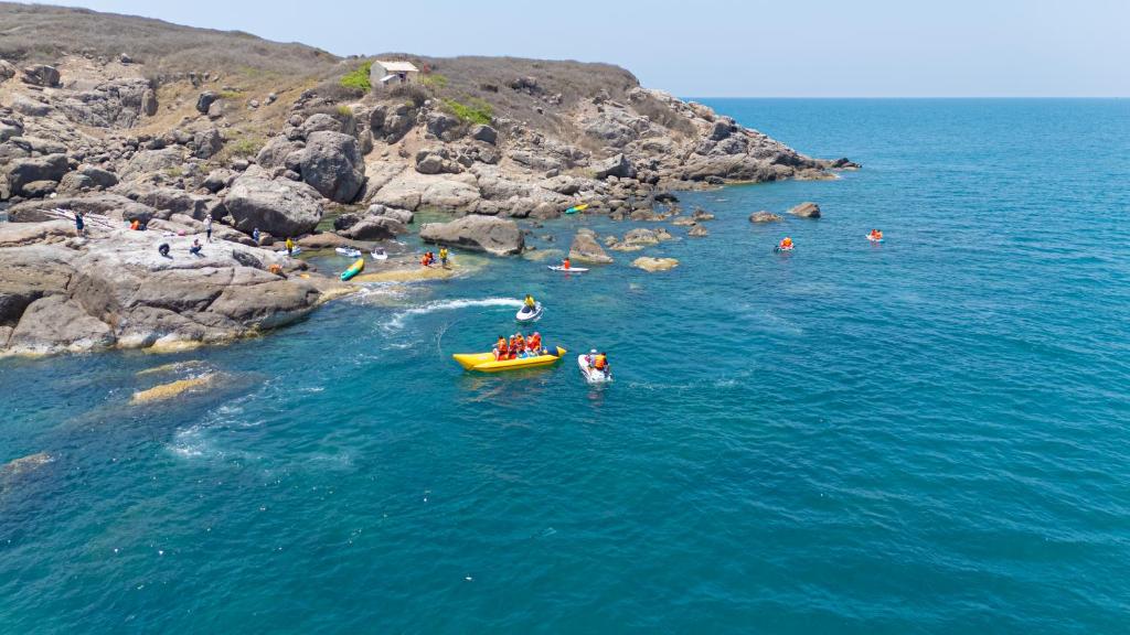 Ūdens aktivitātes pie krasta ar cilvēkiem laivās un uz akmeņiem, skaista jūra un saulaina debess.
