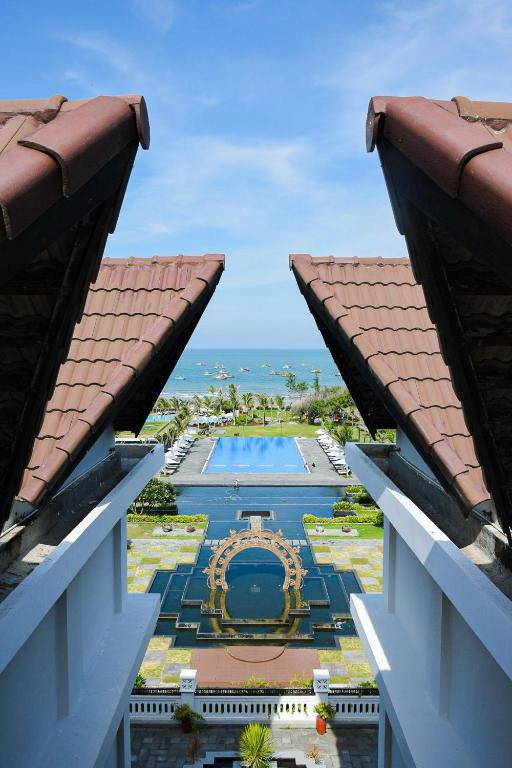 Skats no viesnīcas balkona uz peldbaseinu un okeānu, ar tradicionālām jumtu konstrukcijām abās pusēs.