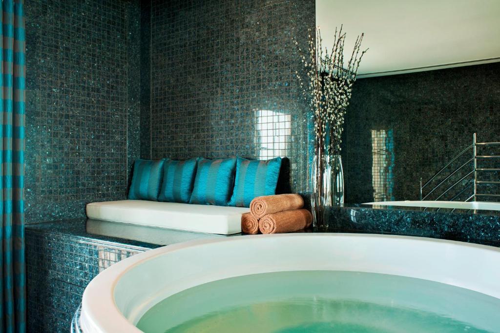 Mūsdienīga spa telpa ar relaksējošu vannu, greznam sēdeklim un dekoratīvām puķēm. Eleganta interjera dizaina elementi rada mierīgu atmosfēru.