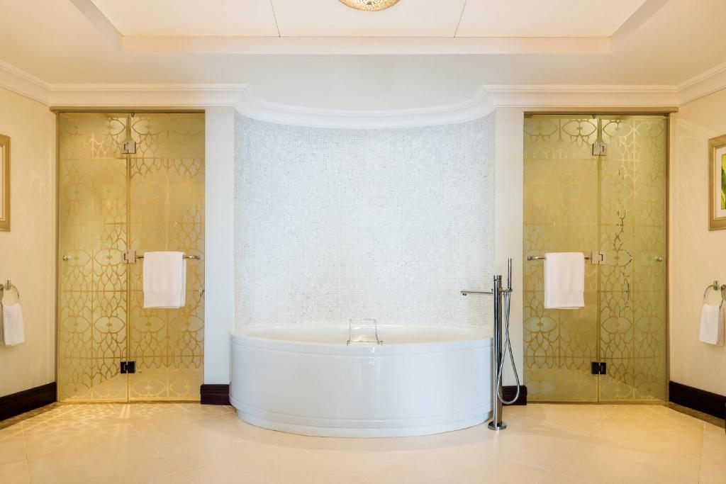 Moderns vannas istabas interjers ar elegantu apaļu vannu un caurspīdīgām zeltītām durvīm, kas piešķir telpai greznību. Apspīdēta flīžu grīda un dekoratīvs sienas apdare rada relaksējošu atmosfēru.