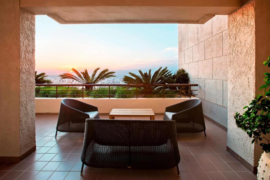 Terase pie Sheraton Rhodes Resort ar skatu uz saulrietu un palmu kokiem.