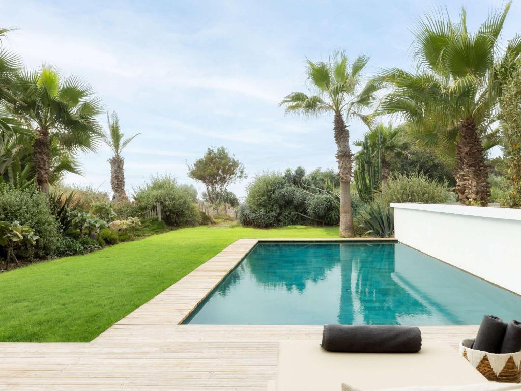 Mūsdienīgs baseins ar apkārtējo dārzu, kurā redzami palmu koki un zāliens, nodrošina mierīgu atpūtas vietu. Ideāls dizains relaksācijai un atpūtai.