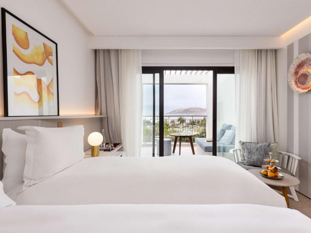 Mūsdienīgs viesnīcas numurs ar divām gultām, gaišām krāsām un panorāmas skatu uz ārpusi. Numurā ir arī balkons ar ērtu sēdvietu un augļu uzkodu.