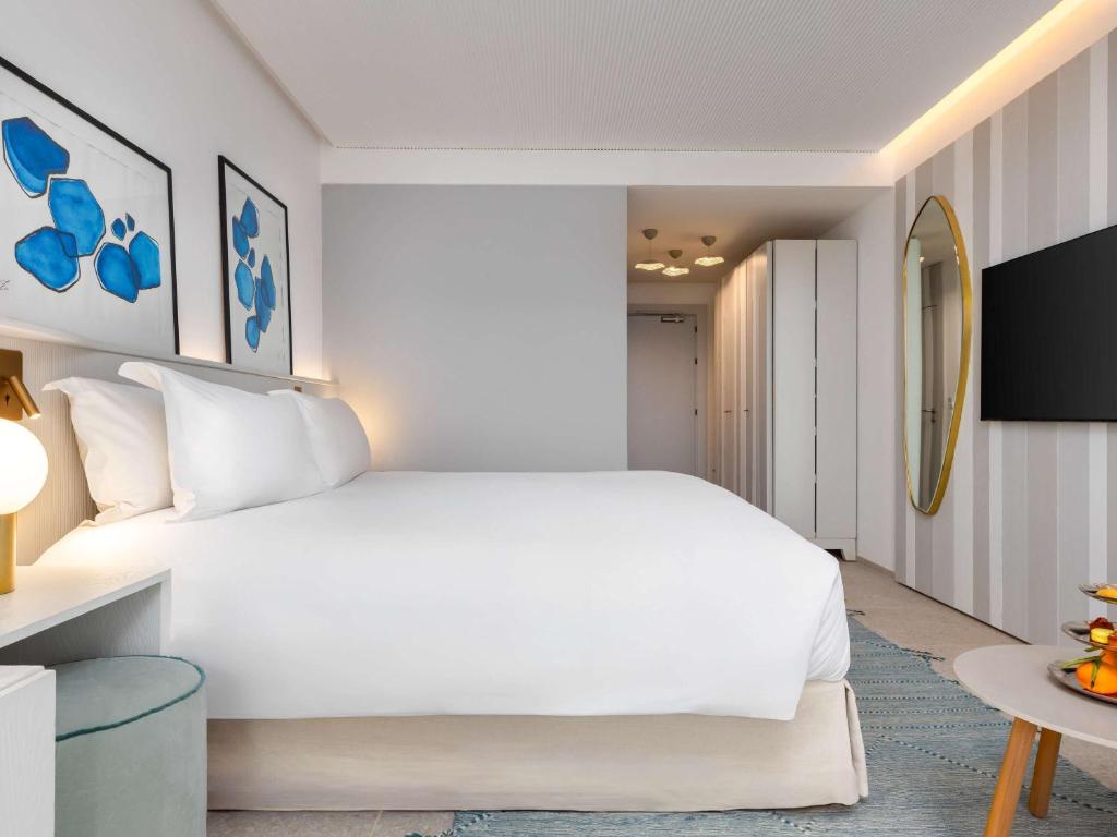 Mūsdienīgs viesnīcas numurs ar plašu gultu, dekoratīviem zila toņa mākslas darbiem uz sienām un elegantu interjeru. Numurā ir arī liels spogulis un televizors, radot komfortablu un estētisku atmosfēru.