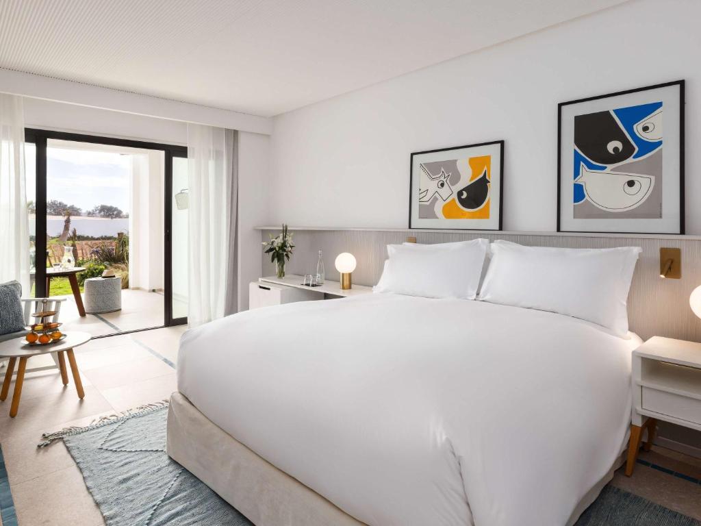 Mūsdienīga guļamistaba ar lielu gultu, mākslas darbiem uz sienām un skatu uz dārzu caur stikla durvīm. Telpa ir gaiša un gaumīgi iekārtota ar komfortablu mēbelēm.