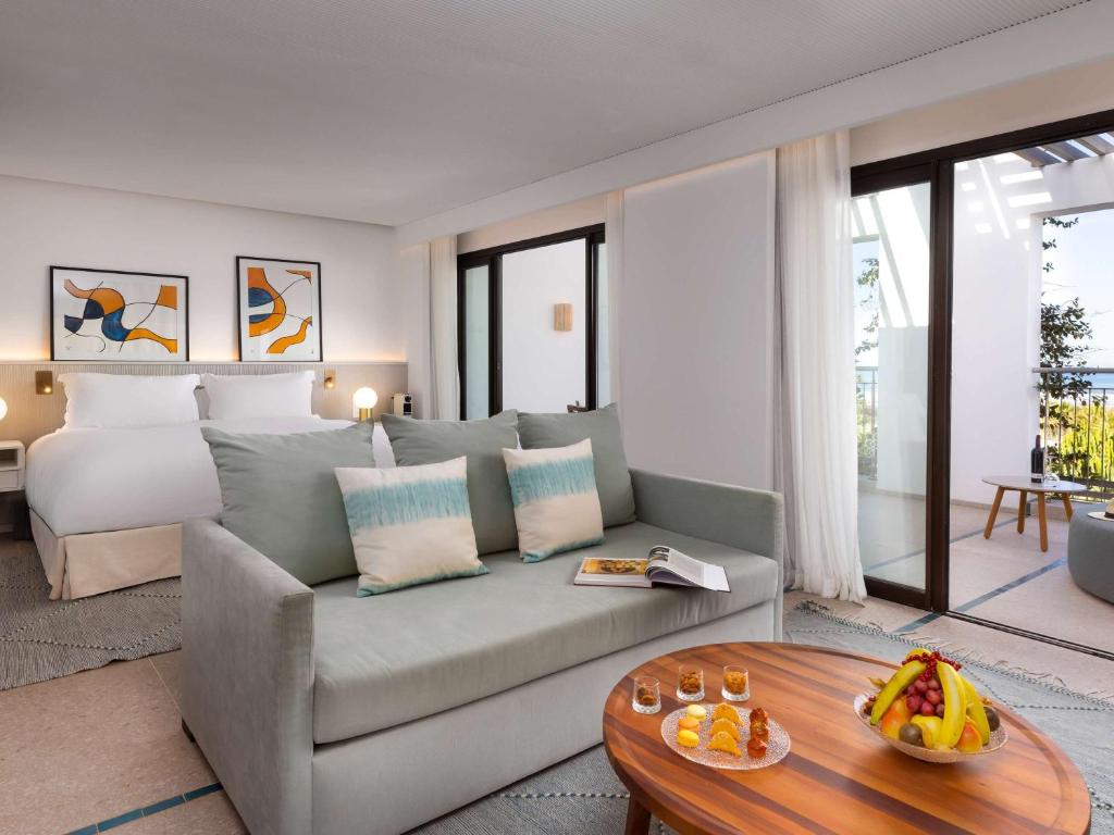 Mūsdienīgs viesnīcas numurs ar gaisīgu interjeru, ērtu dīvānu un izsmalcinātiem mākslas darbiem uz sienām. Uz galda atrodas augļi un uzkodas, radot viesmīlīgu atmosfēru.