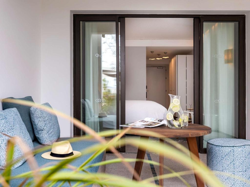 Mūsdienīgs viesnīcas numuriņš ar ērtu dīvānu, galdiņu un dekoratīvu ūdens trauku, kas papildina relaksējošo atmosfēru. Skats uz iekštelpu un ārpusi, radot harmonisku vidi.