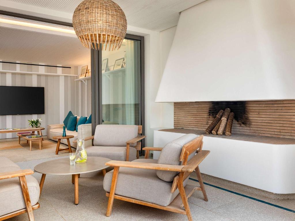 Mūsdienīgs dzīvojamās istabas interjers ar ērtām krēslām, apaļu galdu un kamīnu, kas rada siltu atmosfēru. Gaismas ķermenis no rotangpalmas piešķir telpai elegantu izskatu.