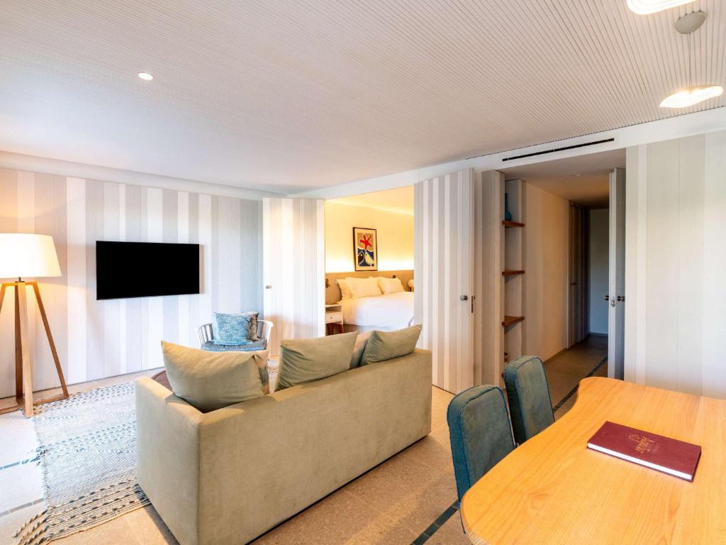 Mūsdienīgs viesnīcas numurs ar viesistabu, kurā ir dīvāns, televizors un galds. Numurs ir gaišs un elegants, ar piekļuvi guļamistabai.