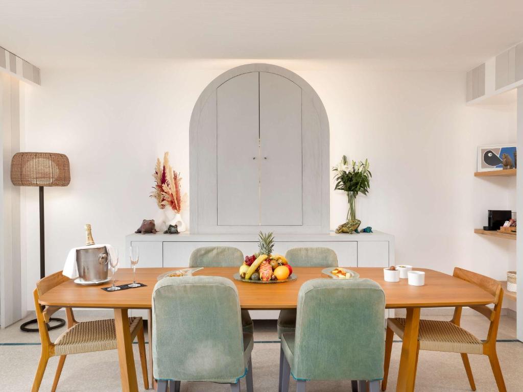 Mūsdienīgs ēdamistabas interjers ar koka galdu, krāsainām augļu dekorācijām un elegantu apgaismojumu. Gaisīgā telpa satur arī ziedus un stilīgu sienas skapi.