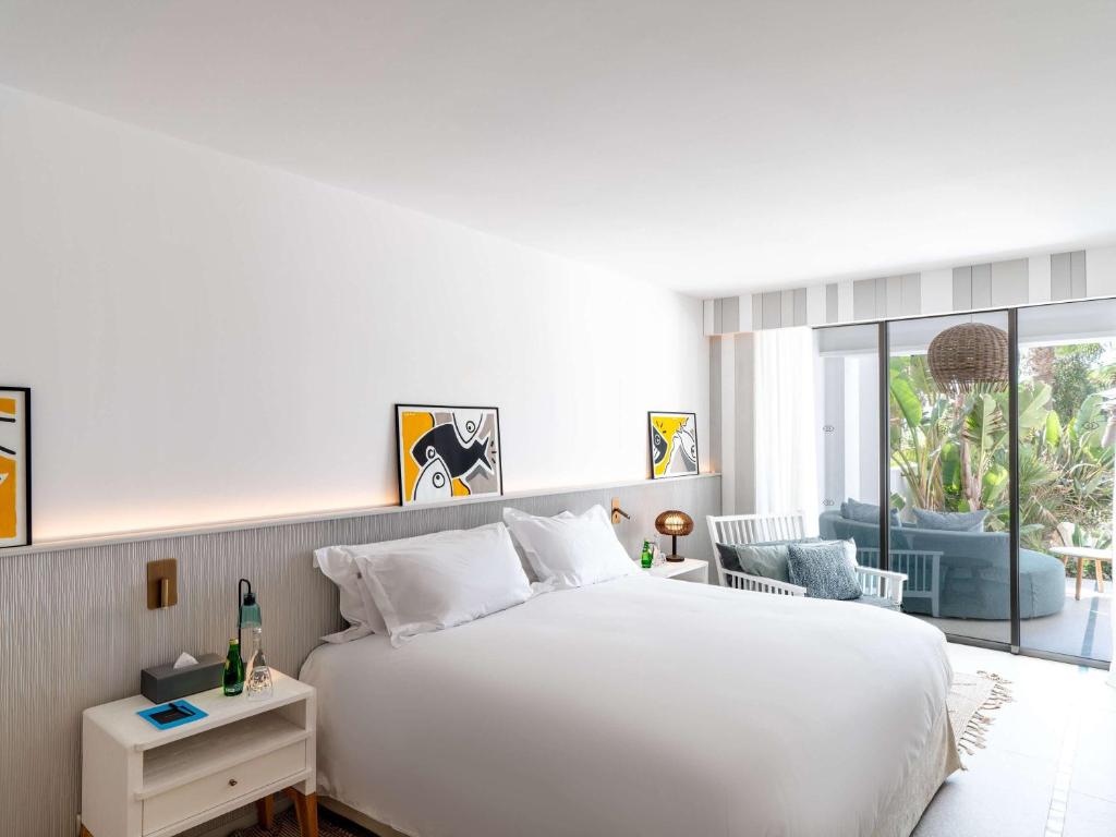 Mūsdienīgs guļamistabas interjers ar plašu gultu, stilīgām gleznām uz sienām un pieejamu terasi, kas ieskauj zaļumi.