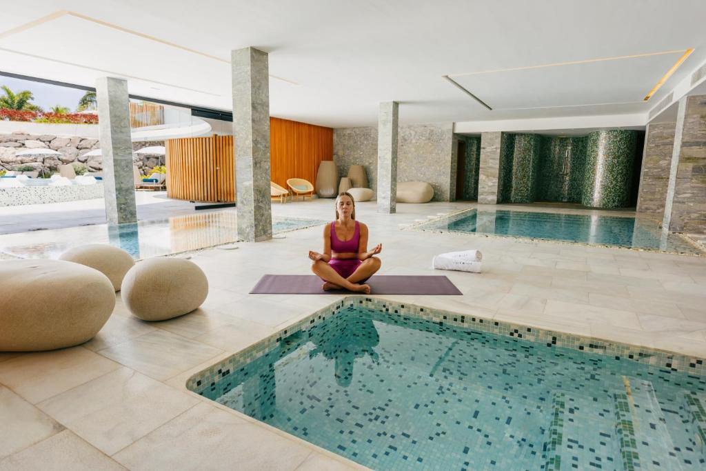 Mūsdienīgs spa interjers ar meditējošu sievieti uz jogas paklājiņa. Apkārt ir relaksējoši ūdens elementi un eleganta arhitektūra.