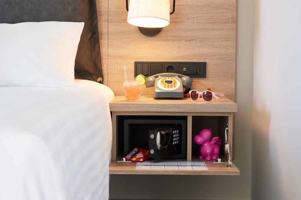 Naktsgaldiņš ar dažādiem priekšmetiem, tostarp telefonu, dzērienu un rozā saulesbrillēm, radot mājīgu atmosfēru viesnīcas numurā. Izcelts arī seifs un rotaļlieta.