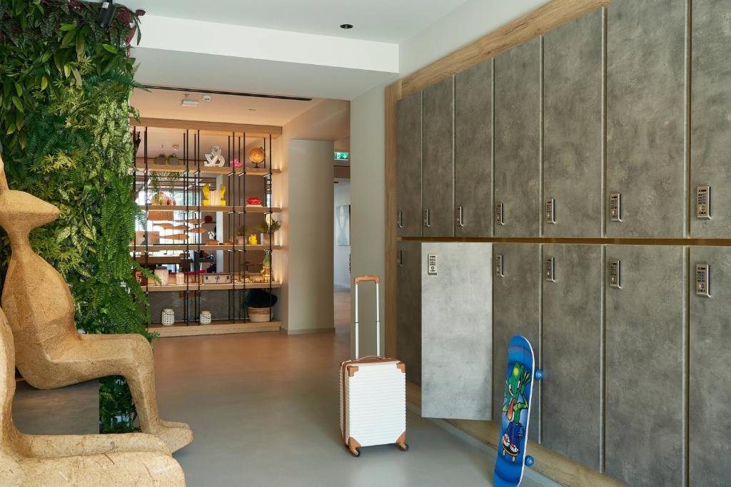 Mūsdienīga telpa ar stilu, kurā redzama zaļa auga siena, skapīši un bagāža, kas gaida savu īpašnieku. Skateboards pie sienas piešķir dzīvīgumu.