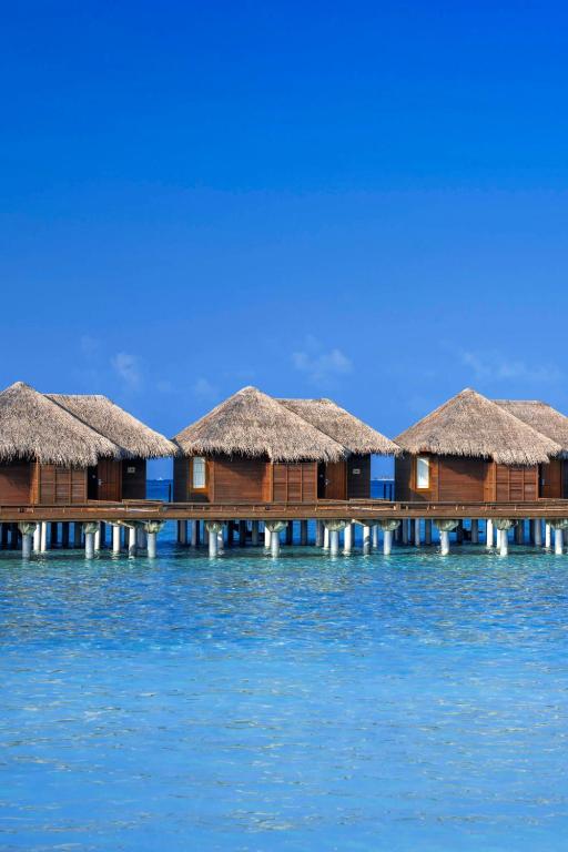 Tropu kūrorts ar koka mājām uz ūdens, kas atrodas kristāldzidros ūdeņos zem skaidras debesīm.
