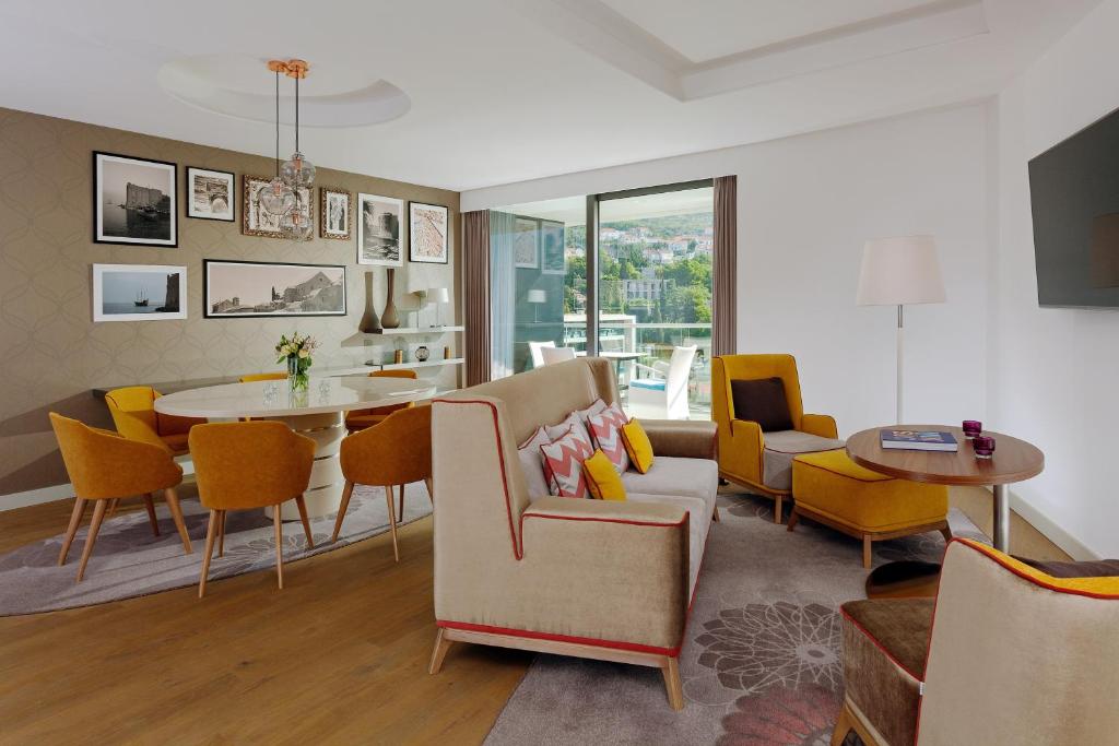 Mūsdienīga viesistaba ar stilīgu interjeru, kurā ir dzeltenas krēsli un eleganta ēdamgalds, papildināta ar mākslas darbiem uz sienām. Logi piedāvā skatu uz dabu, radot patīkamu atmosfēru.