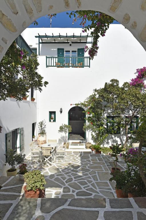 Skaista arhitektūra ar baltām sienām un zaļām durvīm, apzaļumots pagalms ar akmens celiņu un dārza mēbelēm.