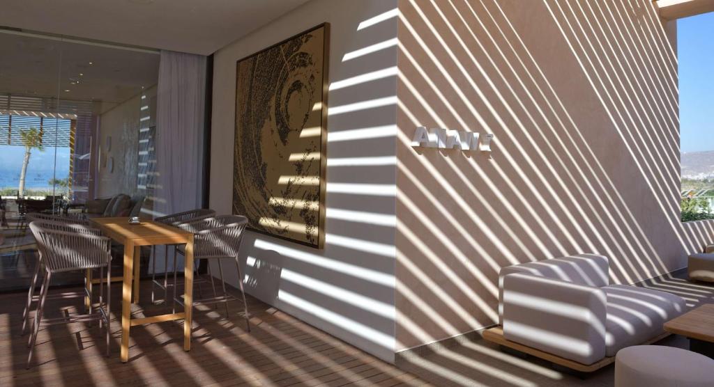 Mūsdienīgs interjers ar koka galdu un krēsliem, ko apgaismo saules stari, kas rada interesantas ēnu līnijas uz sienas. Fons ietver mākslas darbu un skatu uz dabu.