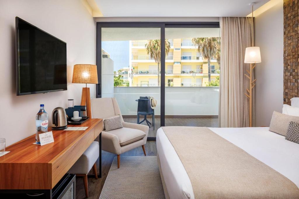 Mūsdienīgs viesnīcas numurs ar plašu logu, kas piedāvā skatu uz terasi. Interjers ir elegants, ar koka mēbelēm un ērtu atpūtas krēslu.