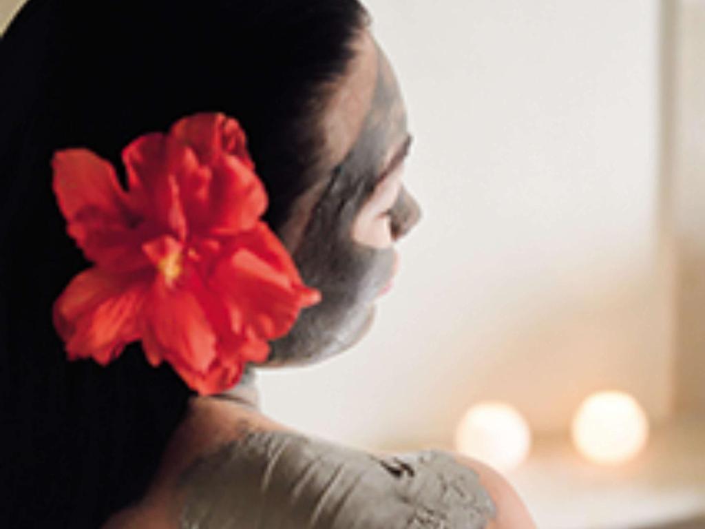 Sieviete ar sejas masku un sarkanu ziedu matos, relaksējoties. Fons ir mierīgs ar izkliedētām gaismām.