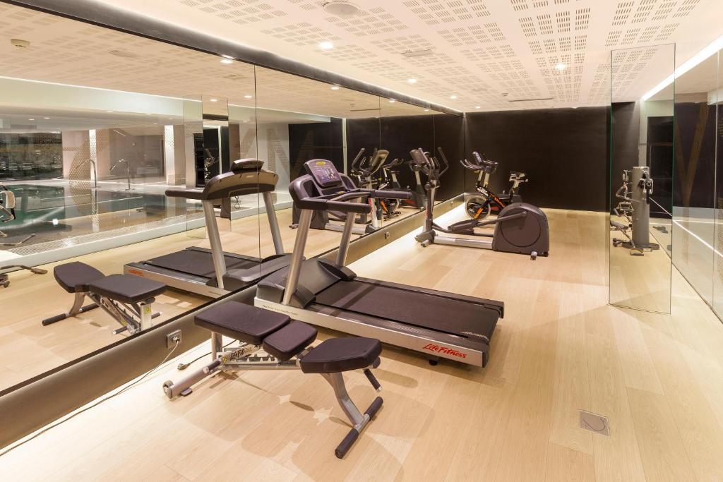 Mūsdienīgs sporta zāles interjers ar dažādām kardio trenažieriem un lielu spoguli. Telpa ir gaiša un plaša, radot motivējošu vidi vingrošanai.