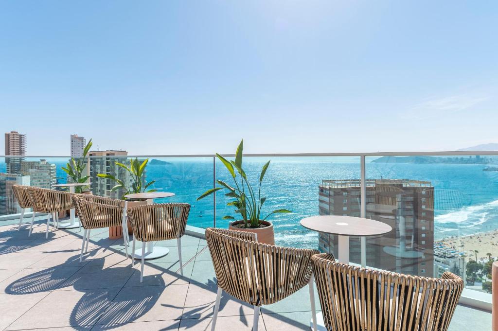 Terases zona ar modernām rattan krēslām un galdiem, skats uz jūru un pilsētas ainavu. Saulains laiks un skaidrs debesis rada relaksējošu atmosfēru.