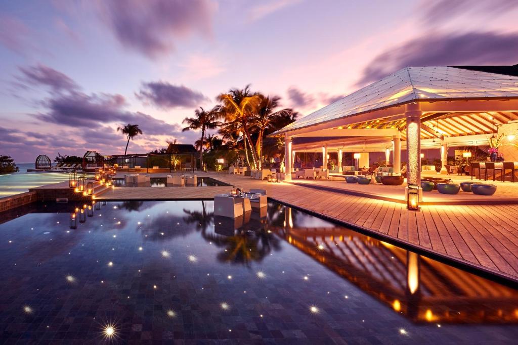 Elegants kūrortviesnīcas terases skats pie saulrieta ar baseinu un palmām. Mierīgs un romantisks atmosfēras noskaņojums ar gaismas elementiem.