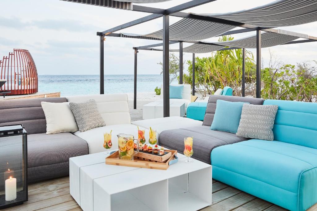 Mūsdienīgs ārējais atpūtas stūrītis ar ērtām dīvāna mēbelēm un dzirkstošiem kokteiļiem uz galda, skats uz jūru un zaļu apkārtni.