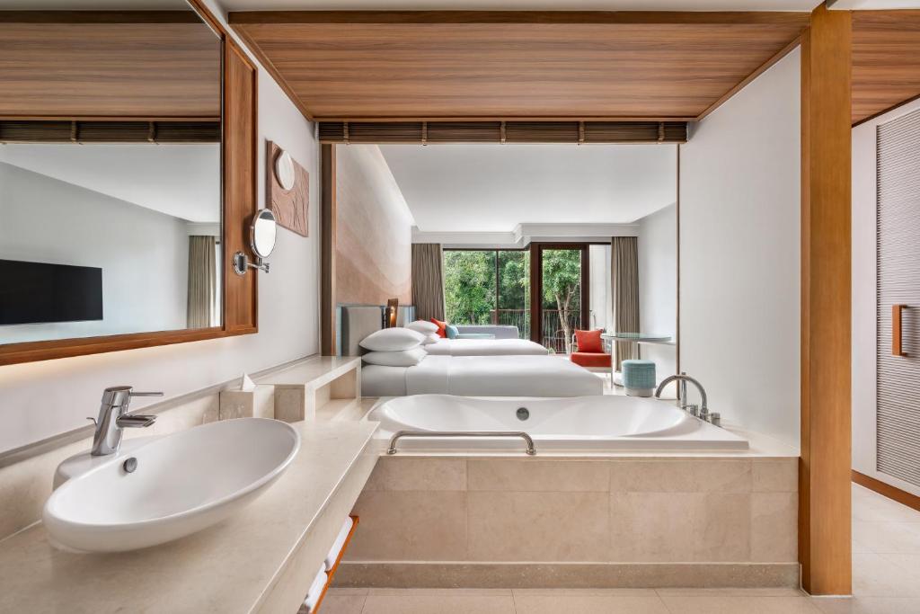 Moderns vannas istabas interjers ar elegantu vannu, divām izlietnēm un skatu uz dārzu caur lieliem logiem. Dabiska gaisma piepilda telpu, radot relaksējošu atmosfēru.