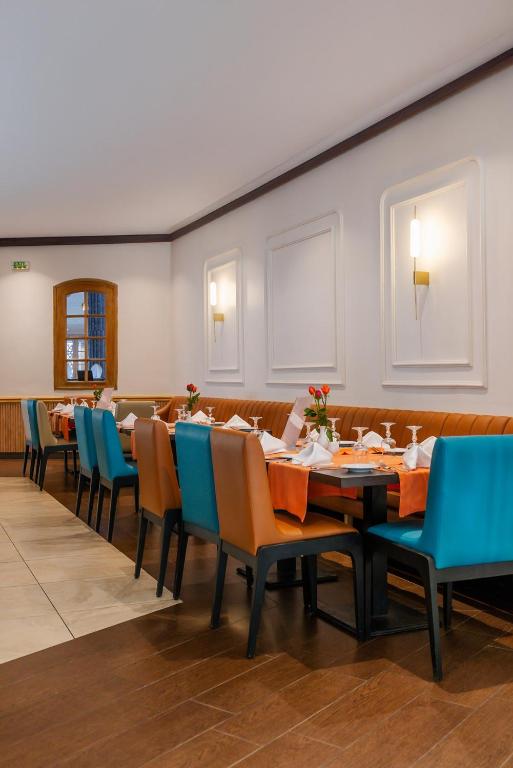 Mūsdienīga restorāna iekārtojums ar krāsainām krēslām, galdiem un dekoratīvām detaļām. Interjers ir gaišs un stilīgs, radot patīkamu atmosfēru.