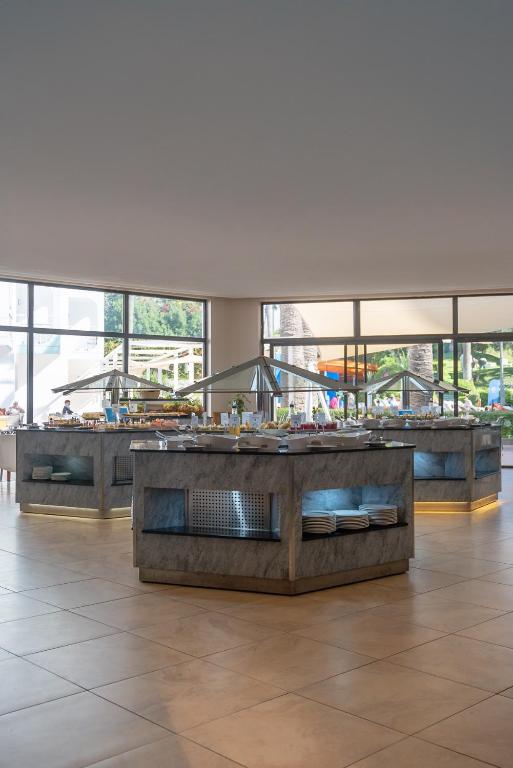 Mūsdienīgs restorāns ar elegantām bufetes stacijām, kurās ir dažādi ēdieni un dzērieni, apgaismots ar mīkstu gaismu. Lielie logi piedāvā skatu uz ārējo vidi, radot patīkamu atmosfēru.