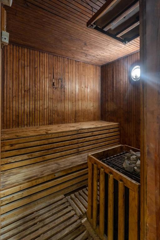 Koka saunas interjers ar sēdvietām un akmeņu krāsni. Mīksts apgaismojums un dabīgas koka detaļas rada relaksējošu atmosfēru.