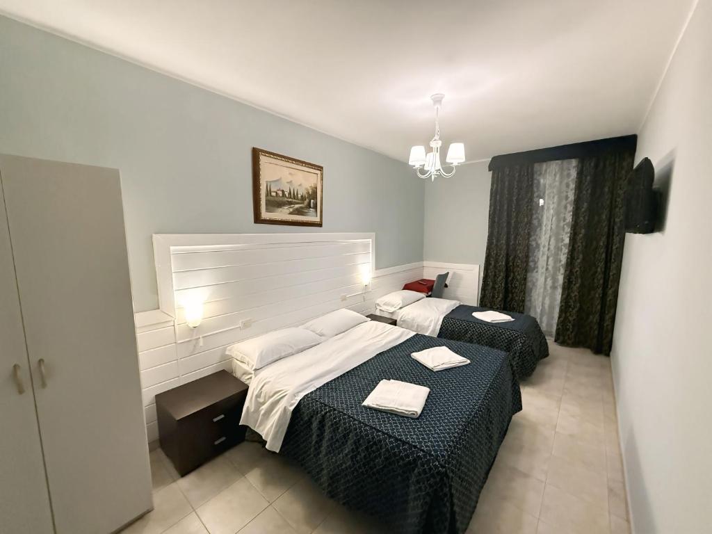 Mūsdienīga viesnīcas numura iekārtojums ar divām gultām, baltiem gultas veļas komplektiem un gleznām uz sienām. Numurs apgaismots ar lustru un logu ar tumšām aizkariem.