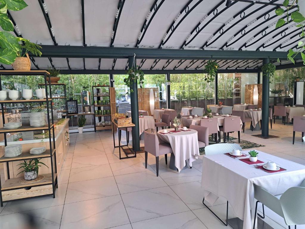 Elegants restorāns ar modernu interjeru, kas ietver augu dekorācijas un mājīgus galdiņus. Gaisīga atmosfēra ar plašām logu virsmām, kas nodrošina dabīgu apgaismojumu.