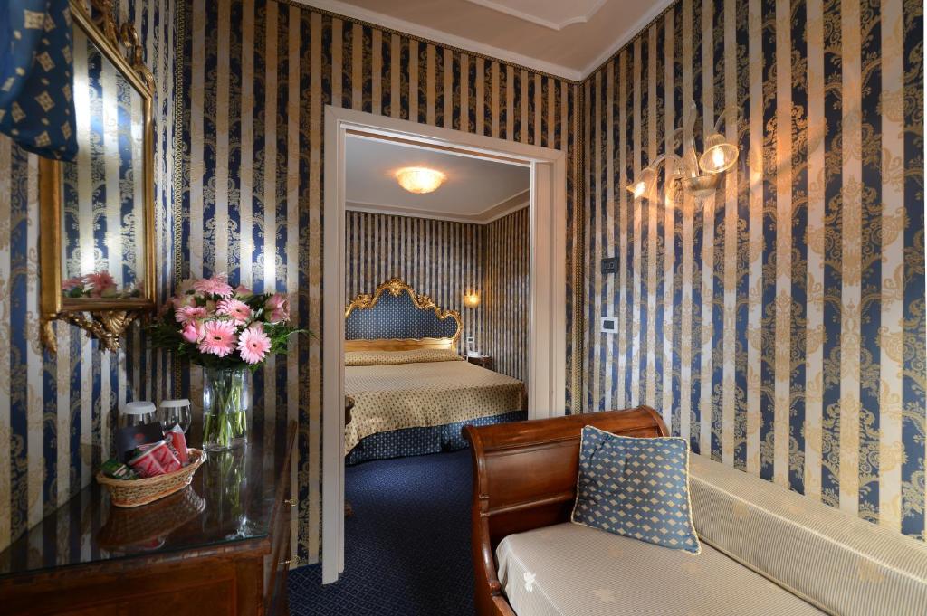 Elegants viesnīcas numurs ar zilu un zelta svītrām, greznu gultu un ziedu kompozīciju uz galda. Interjers ir stilīgs un mājīgs, radot patīkamu atmosfēru.