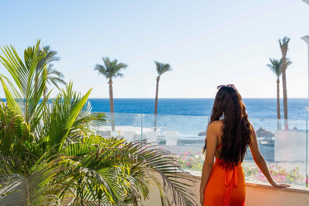 Sieviete vēro skatu uz jūru no Sunrise Remal Beach Resort balkona, apkārt palmām.