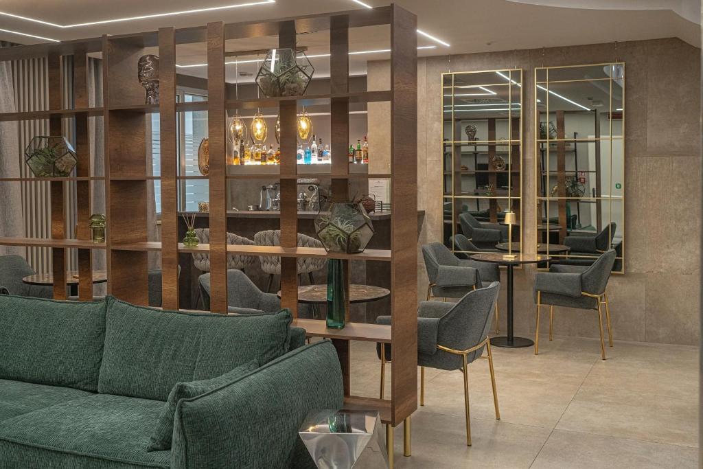 Mūsdienīga viesnīcas uzgaidāmā telpa ar zaļu dīvānu, elegantiem krēsliem un bāru, kas piedāvā plašu dzērienu klāstu. Interjers ir stilīgs un siltas krāsas, radot viesmīlīgu atmosfēru.