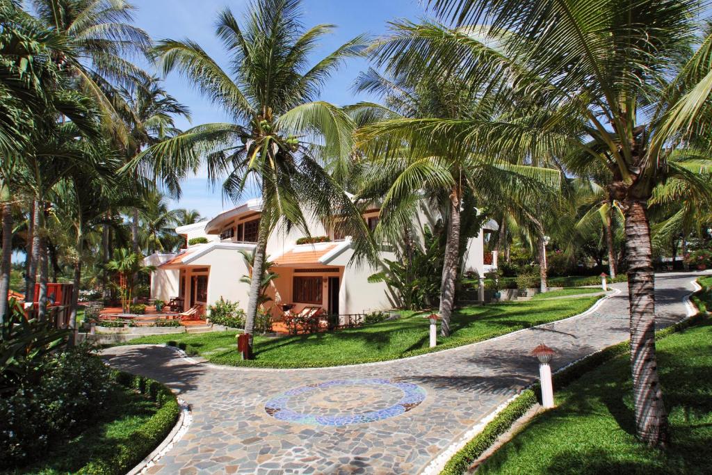 Tropiskā villa, ko ieskauj palmas un zaļš dārzs, ar akmens ceļu, kas ved pie ieejas. Ideāla vieta atpūtai un relaksācijai.