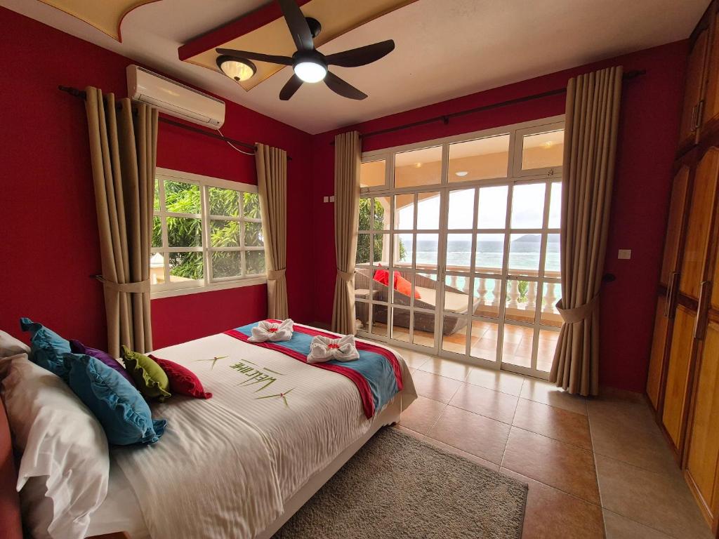 Svaigi iekārtota guļamistaba ar sarkanu sienu, plašu logu un skatu uz jūru. Gultā dekoratīvas spilveni un viegli pieejama terase.