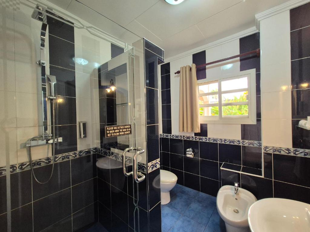 Mūsdienīga vannas istaba ar dušu, tualeti un bidē, kurā dominē melnbaltas flīzes un logs ar skatu uz dārzu.