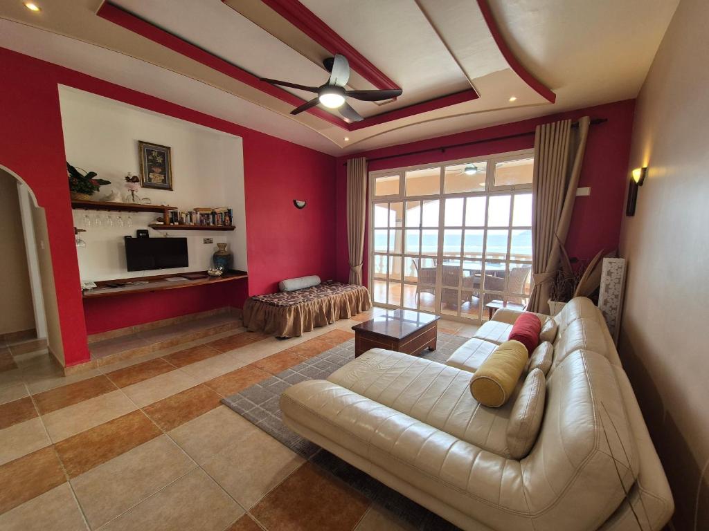 Mūsdienīgs viesistabas interjers ar sarkanu sienu, modernu dīvānu un liela loga skatu uz āru. Telpā ir arī televizors, grāmatu plaukts un elegants apgaismojums.