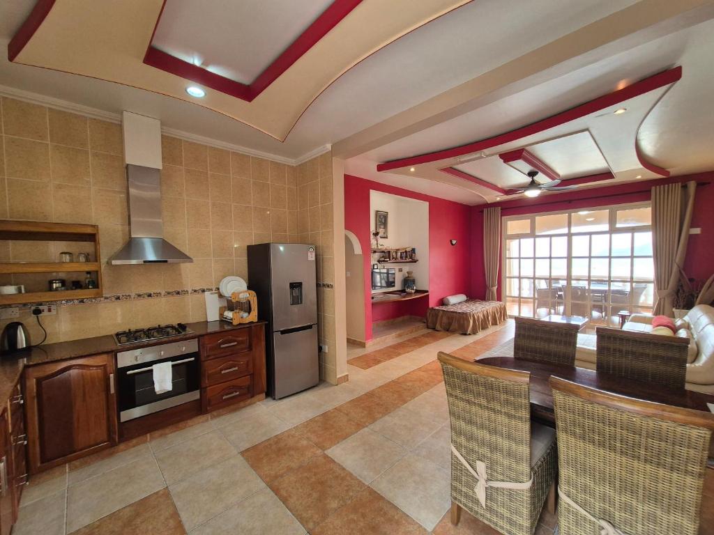 Mūsdienīga atvērta plānojuma virtuve un viesistaba ar koka mēbelēm un gaišām krāsām. Telpai ir lieli logi, kas nodrošina dabisko apgaismojumu un skatu uz ārpusi.