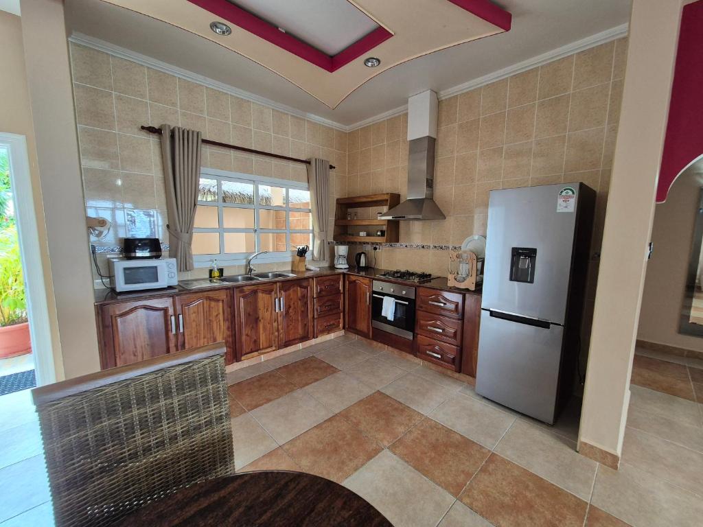 Mūsdienīga virtuve ar koka mēbelēm, metāla ledusskapi un virtuvēm, kas aprīkota ar nepieciešamajiem sadzīves tehnikas priekšmetiem. Telpā ir daudz gaismas un atvērts plānojums.