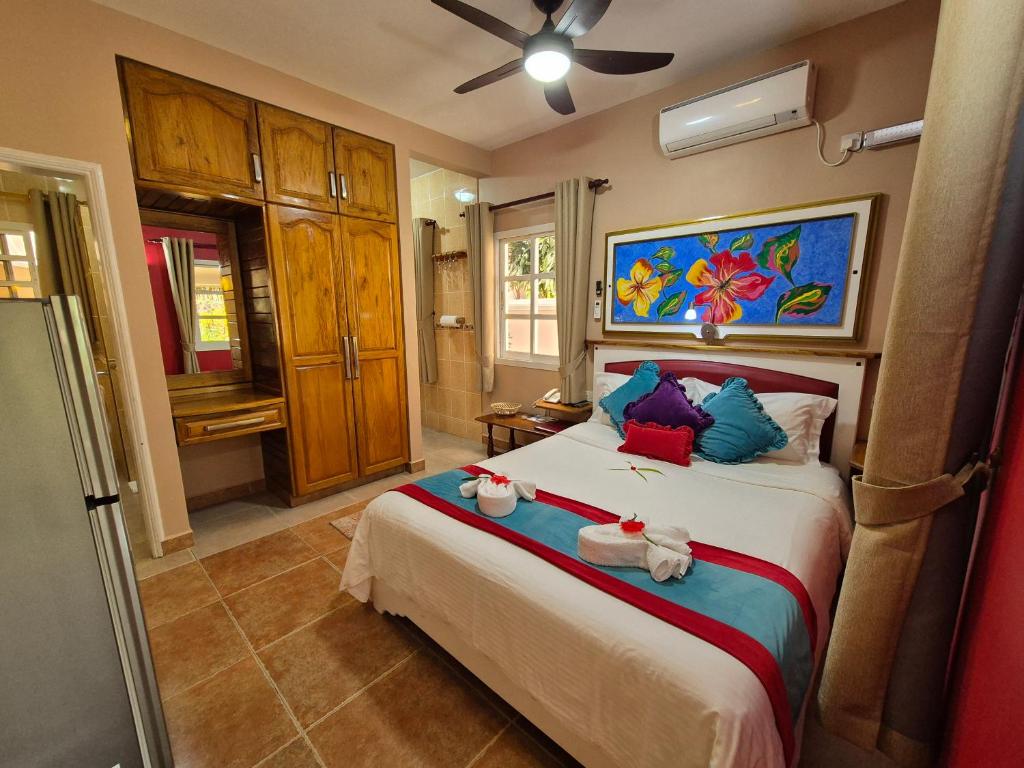 Mūsdienīga guļamistaba ar divvietīgu gultu, koka mēbelēm un krāsainu mākslas darbu pie sienas. Telpā ir gaisa kondicionētājs un silti toņi, radot mājīgu atmosfēru.