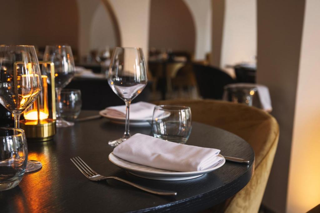 Elegantā restorāna galda uzstādījums ar glāzēm, svečturi un galdautu, radot patīkamu atmosfēru. Ideāls skats romantiskām vakariņām vai svinībām.