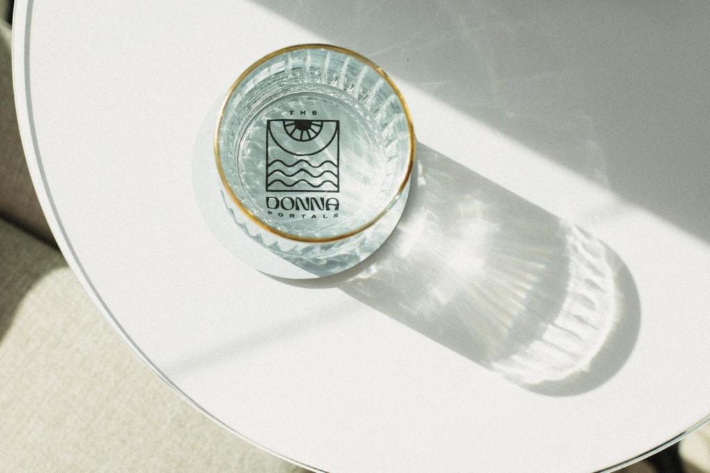 Stikla trauks ar "DONNA PORTALS" logotipu uz baltas virsmas, radot interesantu ēnas efektu.