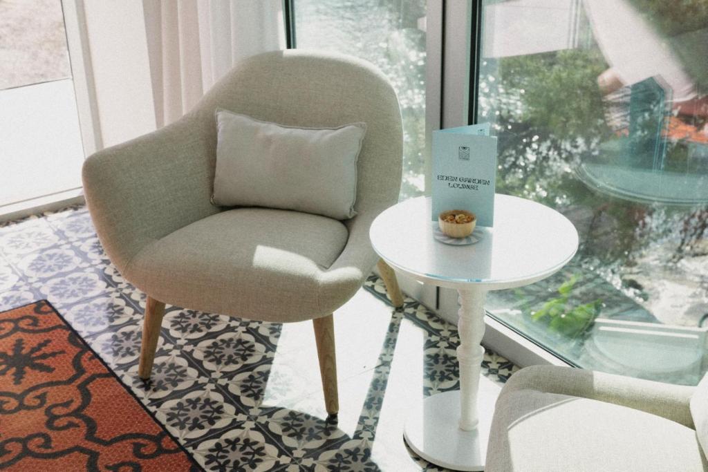 Mūsdienīga atpūtas telpa ar ērtu krēslu un baltu galdu, uz kura atrodas žurnāls un uzkodu trauks. Gaisīga atmosfēra ar dabīgu apgaismojumu un stilīgu grīdas segumu.